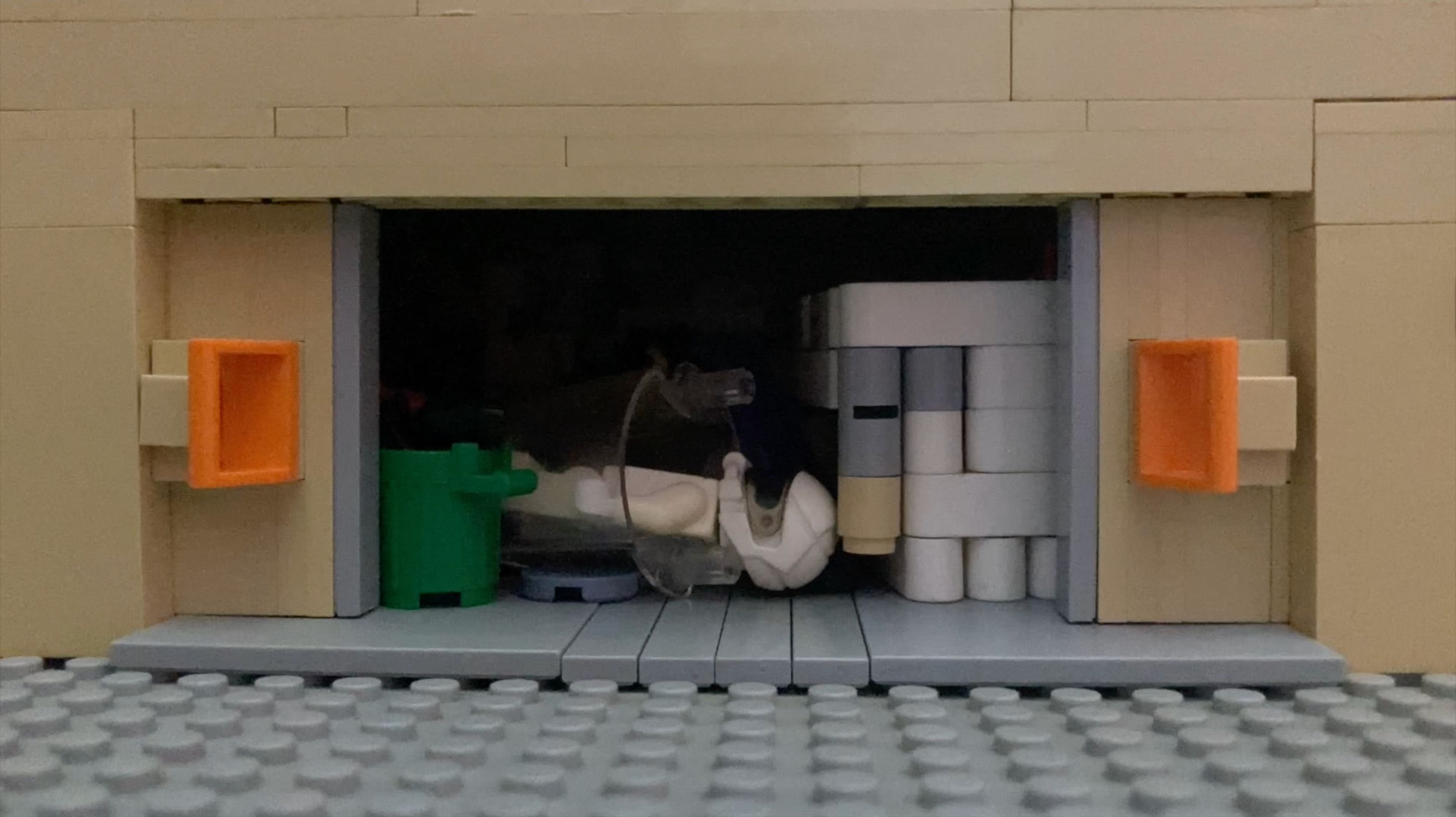 4e photographie de Back to the Moon où les portes du garage d'une maison beige sont ouvertes. Dedans se trouvent une poubelle, une plaque, un costume d'astronaute et un bout de vaisseau spatial.